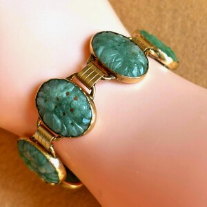 May include: A vintage bracelet featuring oval, carved jade stones in a light green hue, set in gold-toned metal. The jade stones have a floral design. The bracelet is connected by gold-toned links.