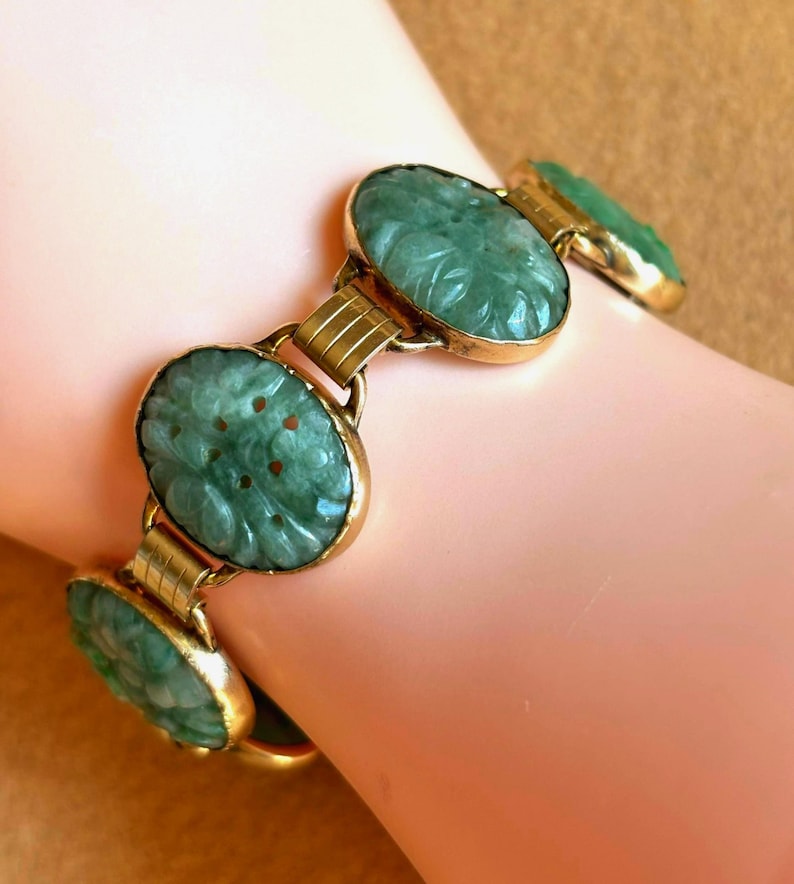 May include: A vintage bracelet featuring oval, carved jade stones in a light green hue, set in gold-toned metal. The jade stones have a floral design. The bracelet is connected by gold-toned links.