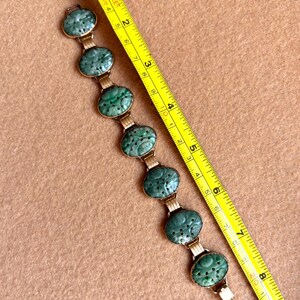 May include: A vintage bracelet featuring oval, carved jade stones in a gold-tone setting. The jade is a rich green color, and the bracelet is shown with a measuring tape. The bracelet is approximately 7 inches long.