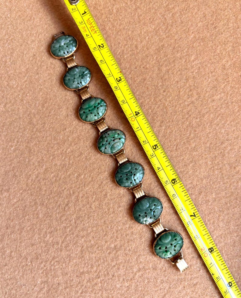 May include: A vintage bracelet featuring oval, carved jade stones in a gold-tone setting. The jade is a rich green color, and the bracelet is shown with a measuring tape. The bracelet is approximately 7 inches long.