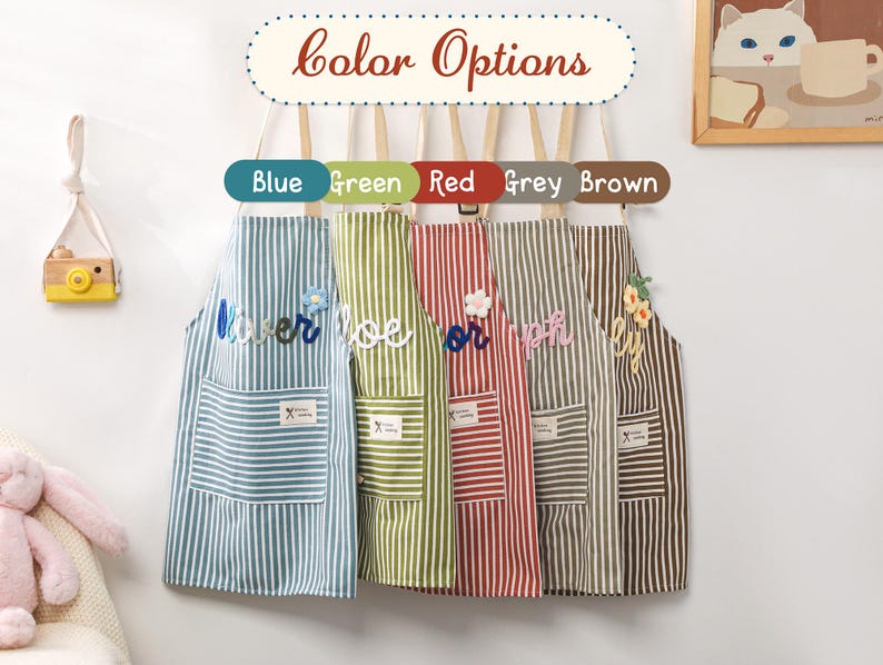 May include: Five striped aprons in blue, green, red, grey, and brown hang on a wooden rack. Each apron has a pocket and a decorative element. The sign above reads "color Options".