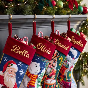 May include: Four needlepoint Christmas stockings with red velvet cuffs, each embroidered with the names Bella, Olivia, David, and Sophia. The stockings feature festive designs including Santa Claus, a polar bear, a nutcracker, and a steam train.