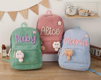 May include: Three personalized corduroy backpacks with embroidered names, Alice, Pudy, and Maria. Each backpack features a small plush animal charm.