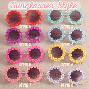 May include: Eight pairs of round sunglasses arranged in a grid, each featuring a frame decorated with small daisy flowers. The colors include red, light blue, purple, light blue, pink, yellow, peach, and white. Each pair is labeled Style 1 through 8.