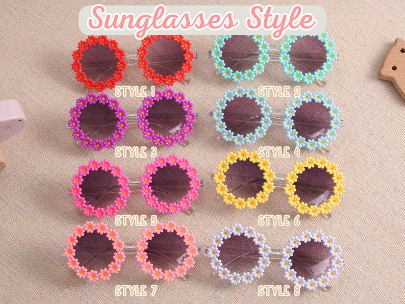 May include: Eight pairs of round sunglasses arranged in a grid, each featuring a frame decorated with small daisy flowers. The colors include red, light blue, purple, light blue, pink, yellow, peach, and white. Each pair is labeled Style 1 through 8.