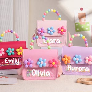 May include: Four small rectangular handbags in shades of hot pink, light pink, and lavender. Each bag features a clear front pocket with colorful confetti, a top handle made of multi-colored beads, and three plastic flower appliques.
