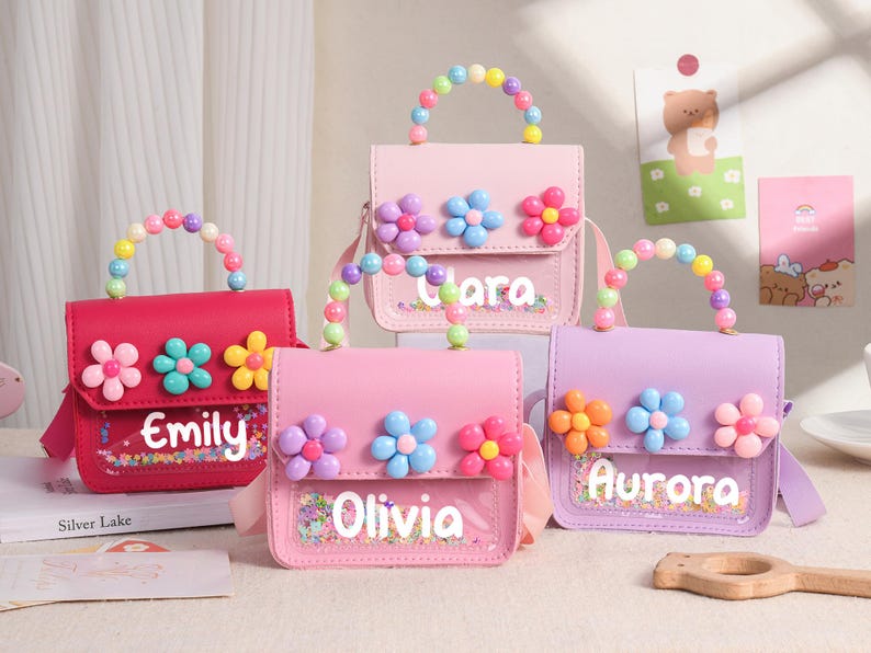 May include: Four small rectangular handbags in shades of hot pink, light pink, and lavender. Each bag features a clear front pocket with colorful confetti, a top handle made of multi-colored beads, and three plastic flower appliques.