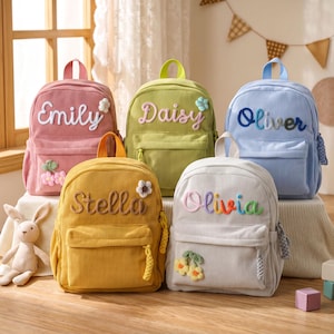 May include: Five corduroy backpacks in pink, lime green, light blue, yellow, and light grey. Each bag features a front pocket, a top handle, and a personalised name embroidered in cursive script. Decorative fabric flowers are attached to the bags.