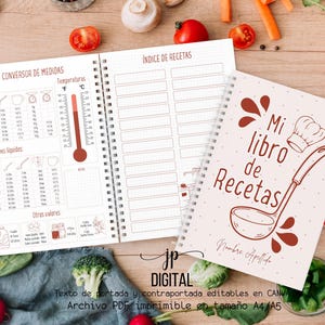 Pode incluir: Um livro de receitas com encadernação em espiral, com o texto "Mi libro de Recetas" na capa e uma ilustração de concha. As páginas abertas exibem um índice de receitas e uma tabela de conversão de medidas. Vegetais frescos circundam o livro.