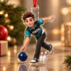 May include: A clear acrylic Christmas ornament featuring a cartoon-style character bowling. The character wears a teal and black shirt with the name OWEN and the year 2026 printed on it, black pants, and white shoes. A blue bowling ball and two pins are included.