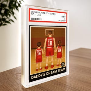 May include: A framed print from the 2025 Exquisite Collection, featuring a basketball-themed illustration. The image shows a father and two children in red basketball uniforms, with the text "DADDY'S DREAM TEAM" at the bottom. The print is encased in a clear protective case.