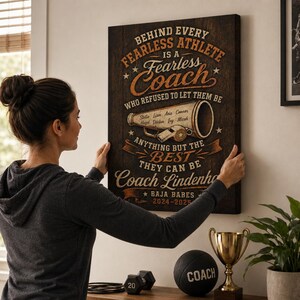 May include: A rectangular wall canvas with a dark wood grain background featuring the text: BEHIND EVERY FEARLESS ATHLETE IS A Fearless Coach WHO REFUSED TO LET THEM BE ANYTHING BUT THE BEST THEY CAN BE Coach Lindenho BAJA BABES 2024-2025.