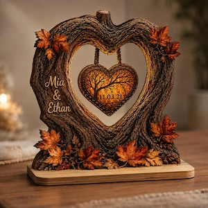 May include: A heart-shaped tree bark frame with orange and brown autumn leaves, featuring the names Mia & Ethan and a hanging heart ornament with a tree silhouette and the date 11.03.21, all illuminated by a warm internal light on a flat base.