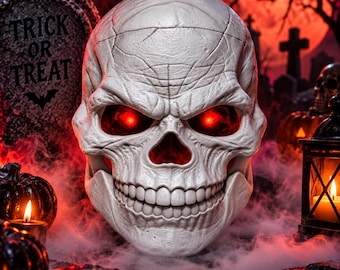May include: A white skull decoration featuring deep-set eye sockets that glow with a bright red light. The skull has a textured surface with visible cracks and a wide, toothy grin, positioned as a central focal point in a dark, atmospheric setting.