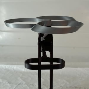 以下が含まれることがあります： ドローンを置くための3Dプリントされた黒と灰色のスタンド。ドローン用の円形ホルダーとコントローラー用の長方形ホルダーがあります。