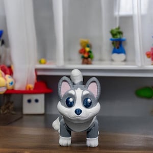 Può includere: Una statuetta di un cane husky grigio e bianco con occhi blu, stampata in 3D. La statuetta è in piedi su una superficie di legno.