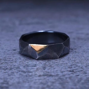 Könnte beinhalten: Ein geometrischer Ring mit einer strukturierten Oberfläche in Schwarz und Gold.