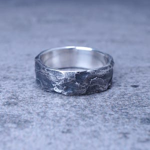 May include: A silver ring with a textured, hammered finish. The ring is wide and has a rounded shape.