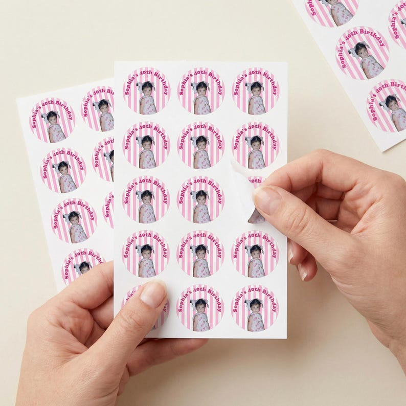 May include: Sheets of round stickers with a photo of a young girl, pink stripes, and the text "Sophia's 40th Birthday." The stickers are being peeled from the sheet. The stickers are for a birthday party.