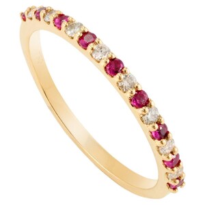 May include: A gold band ring set with alternating red gemstones and clear gemstones. The ring's gemstones are evenly spaced around the band. The ring is made of gold and has a polished finish. The gemstones are small and round.