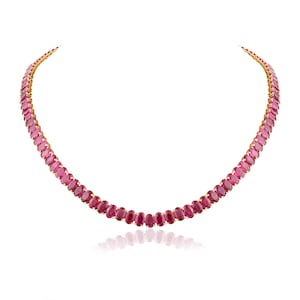Puede incluir: Un collar de oro con una serie de piedras preciosas rojas oscuras de corte ovalado. Las piedras están muy juntas, creando una línea continua de color. El collar se muestra sobre un fondo blanco, resaltando el diseño de la joya.