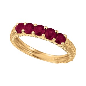 May include: A gold ring with five deep red gemstones. The band has a detailed, textured pattern. The gemstones are set in individual prongs. The ring is displayed against a white backdrop.
