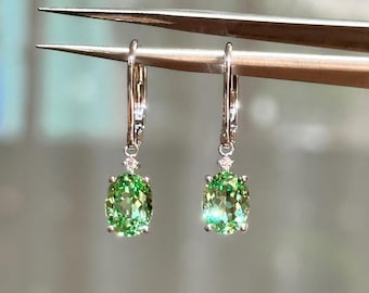 Peut inclure: Une paire de boucles d'oreilles en argent avec des pierres précieuses ovales vert clair. Chaque boucle d'oreille comporte une petite pierre ronde et transparente au-dessus de la pierre verte plus grande. Les boucles d'oreilles sont tenues par une pince à épiler.