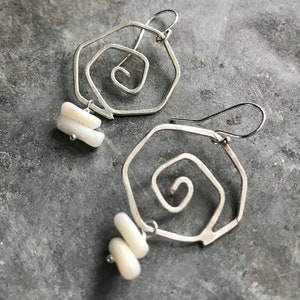 Pode incluir: Brincos de prata com um design em espiral e detalhes de concha branca.