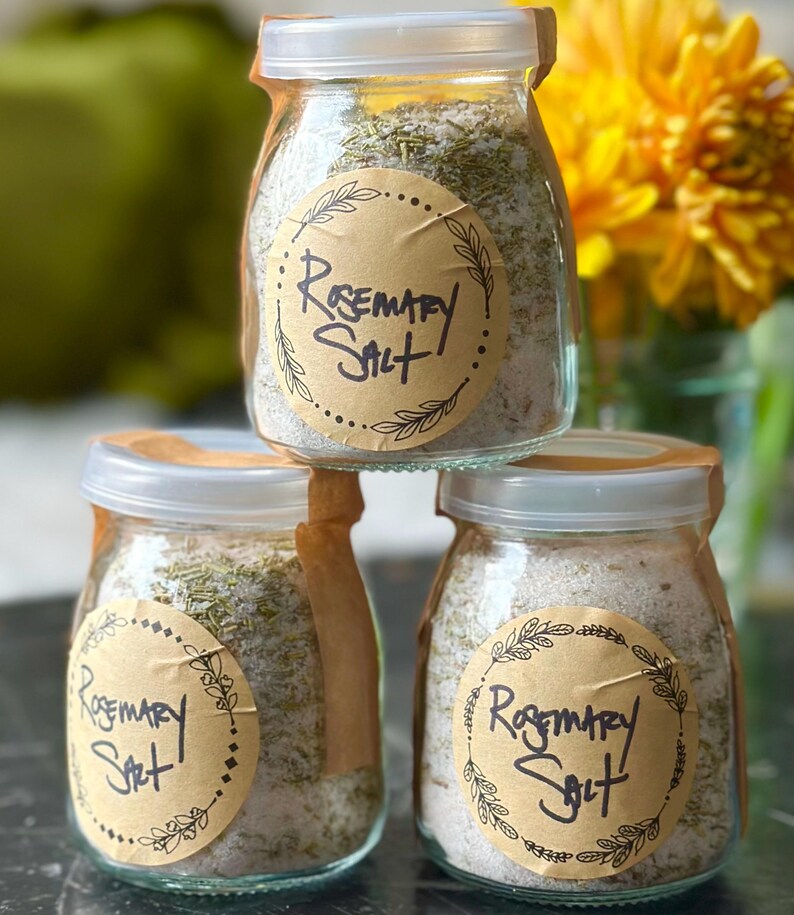 Puede incluir: Tres frascos de vidrio llenos de sal de romero, cada uno con una etiqueta de papel marr&oacute;n que dice "Rosemary Salt".