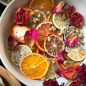Może przedstawiać: Biała miska wypełniona suszonymi plastrami owoców cytrusowych, płatkami róż i lawendą. Owoce cytrusowe obejmują pomarańcze, grejpfruty i limonki.