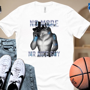 May include: White t-shirt featuring a wolf character wearing a top hat. The shirt has the text "NO MORE" above the wolf and "MR NICE GUY" below. The wolf is depicted in shades of gray and blue.