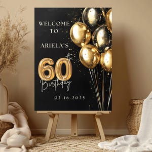 May include: Black welcome sign with gold glitter and balloons. The sign says "Welcome to Ariela's 60th Birthday 03.16.2025".
