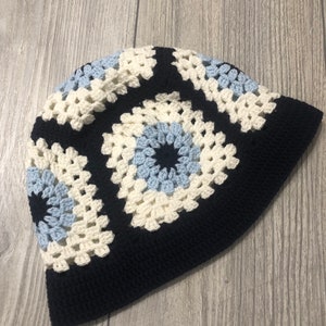 Op de afbeelding: Een zwarte gehaakte muts met witte en blauwe granny squares.