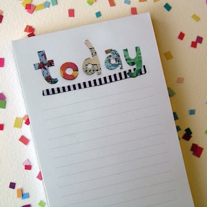 May include: A white notebook with lined paper and the word "today" spelled out in colorful, patterned letters. The letters are made of paper and have a black and white striped border.
