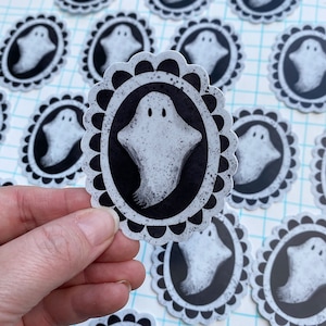 May include: A set of white ghost stickers with black outlines and a black and white patterned frame. The ghosts are in a variety of poses and expressions.
