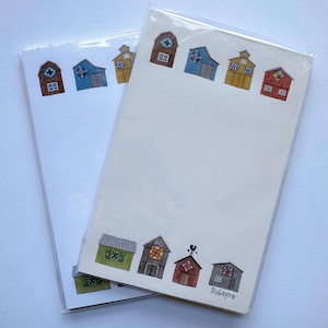 May include: Two notepads with a white background and a colorful barn design. The barns are in various colors, including brown, blue, yellow, and red. The notepads are packaged in clear plastic.