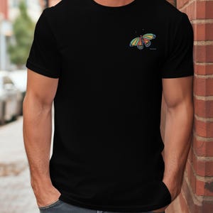 May include: A black t-shirt with a colorful butterfly graphic on the left chest. The butterfly has yellow, orange, red, blue, and green accents.