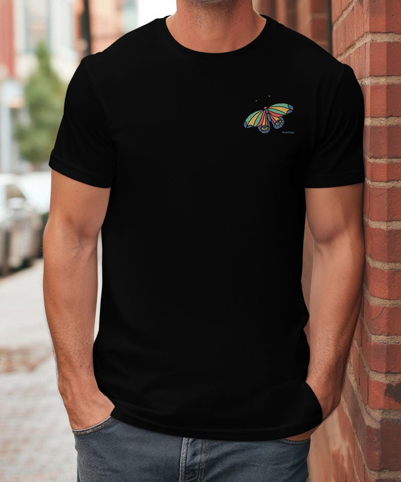 May include: A black t-shirt with a colorful butterfly graphic on the left chest. The butterfly has yellow, orange, red, blue, and green accents.