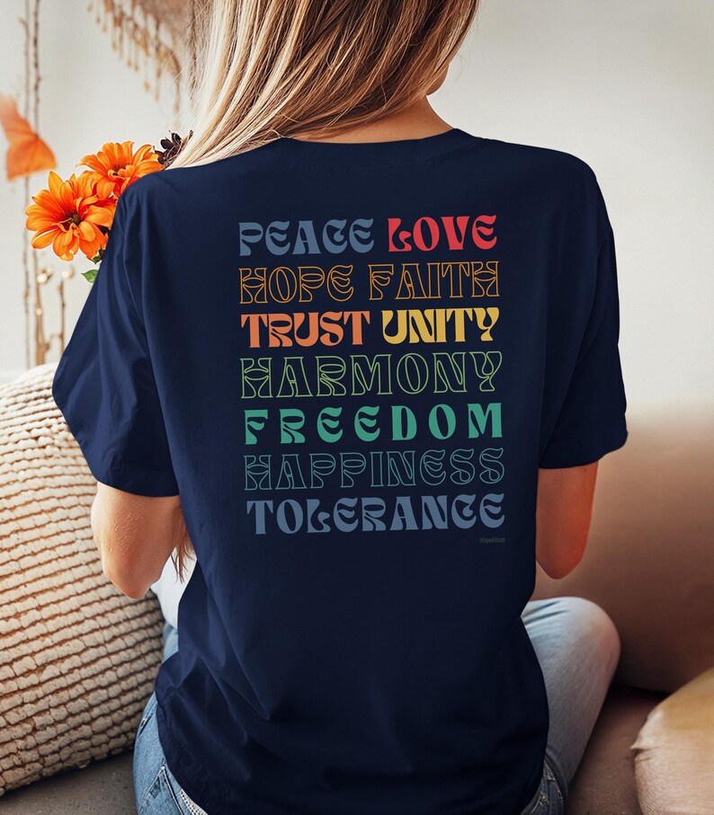 May include: A navy blue t-shirt with a rainbow-colored graphic on the back. The graphic features the words "Peace Love Hope Faith Trust Unity Harmony Freedom Happiness Tolerance".