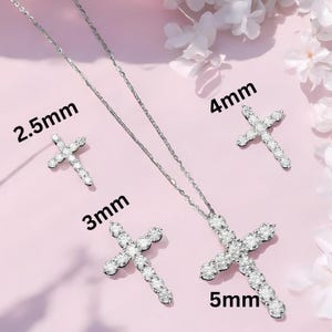 May include: A silver-toned jewelry set featuring cross pendants and earrings. The set includes a necklace with a 5mm cross pendant, a pair of 2.5mm earrings, and two additional crosses measuring 3mm and 4mm. The jewelry is set against a pink background.