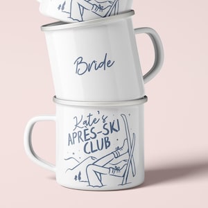 Op de afbeelding: Drie witte emaille mokken op elkaar gestapeld. De bovenste en onderste mokken hebben de tekst "Kate's APRES-SKI CLUB" met een skiër-afbeelding. De middelste mok zegt "Bride". Alle mokken hebben een zilveren rand en handvat.