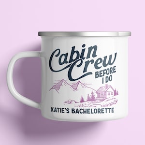 May include: White enamel mug with a silver rim and handle. The mug features the text "Cabin Crew Before I Do" in navy blue script, with a mountain and cabin illustration in purple. The text "Katie's Bachelorette" is below.