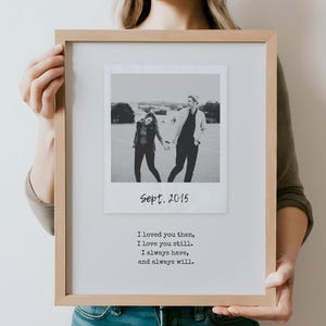 May include: Black and white photo of a couple holding hands in a field. The photo is framed in a light wood frame with a white mat. The text "Sept. 2015" is printed below the photo. The text "I loved you then, I love you still. I always have, and always will." is printed below the date.