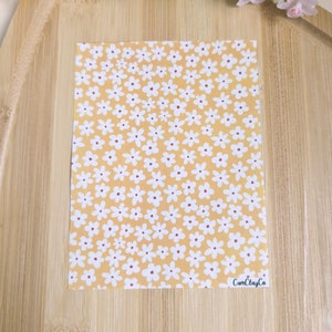 Peut inclure: Une feuille de papier jaune avec un motif de marguerites blanches et des centres rouges. Le papier porte le texte "CarnClayCo" dans le coin inférieur droit.