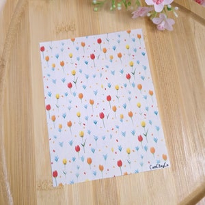 Könnte beinhalten: Ein weißes Blatt Papier mit einem sich wiederholenden Muster aus roten, gelben und blauen Tulpen. Das Papier hat eine subtile Textur und die Tulpen sind in einem einfachen, verspielten Stil gezeichnet. Der Text "CamClayCo" ist in der unteren rechten Ecke gedruckt.
