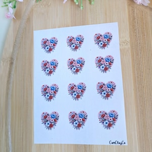 Könnte beinhalten: Ein Bogen Aufkleber mit herzförmigen Blumendesigns. Jedes Herz besteht aus roten, blauen und weißen Blumen. Die Aufkleber befinden sich auf weißem Hintergrund, mit dem Text "CamClayCo" unten rechts.