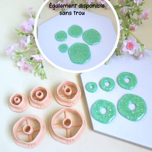 May include: A set of five peach-colored circular clay cutters with central posts, alongside five green glittery circular clay pieces with holes. An inset circle shows five green glittery clay pieces without holes and the text Également disponible sans trou.