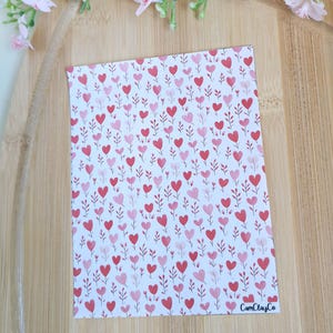 Peut inclure: Une carte rectangulaire avec un motif de cœurs rouges et roses et des éléments floraux sur fond blanc. Le texte "CamClayCo" est visible en bas à droite. Des fleurs roses ornent l'arrière-plan.