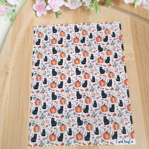 Puede incluir: Una lámina rectangular con un patrón repetido de gatos negros y calabazas naranjas sobre un fondo blanco. El diseño incluye hojas de otoño. El texto "CamClayCo" es visible en la esquina inferior derecha.