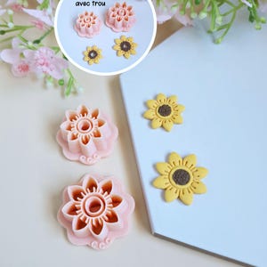 Puede incluir: Dos cortadores de galletas de plástico rosa en forma de flor con un agujero en el centro. Dos girasoles de fondant amarillo con centros marrones.